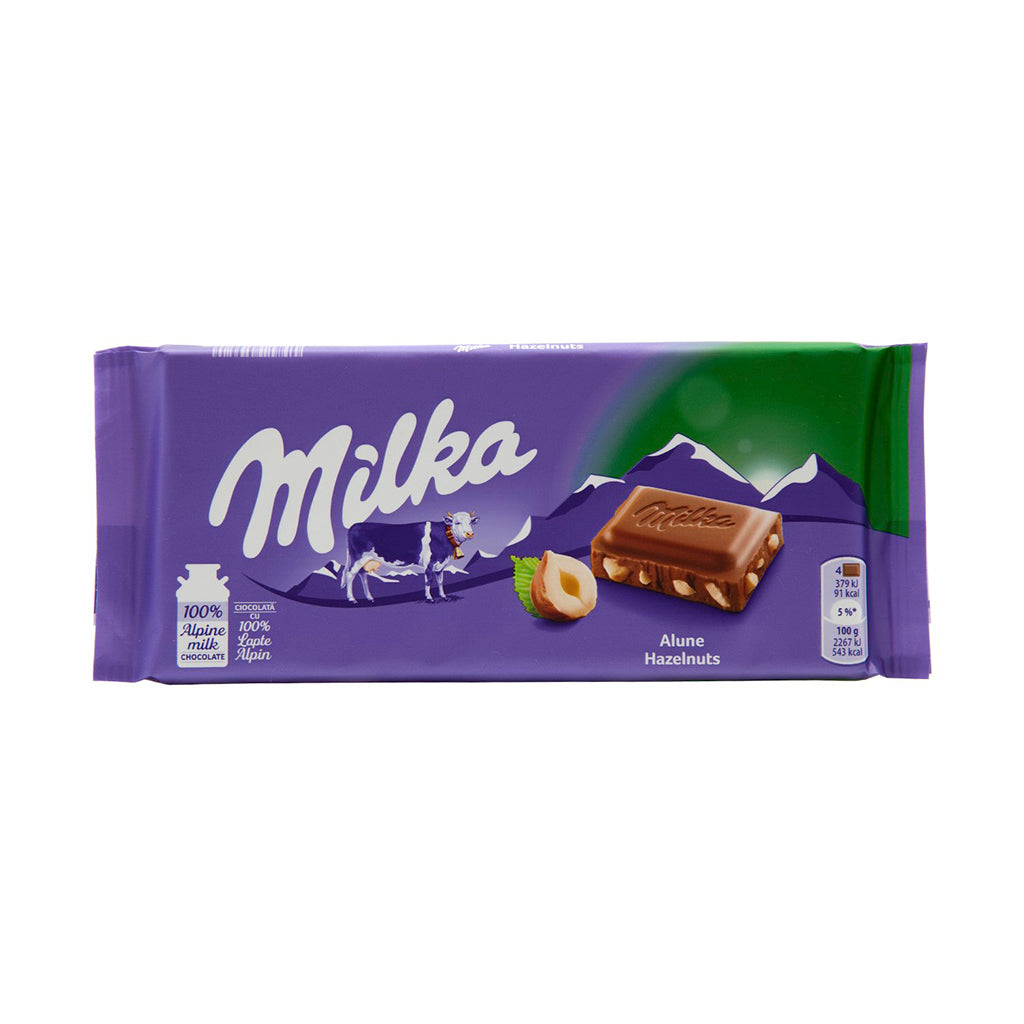 Packaged 100g Milka Hazelnut Chocolate Bar with visible creamy chocolate and whole hazelnuts on a vibrant purple background.